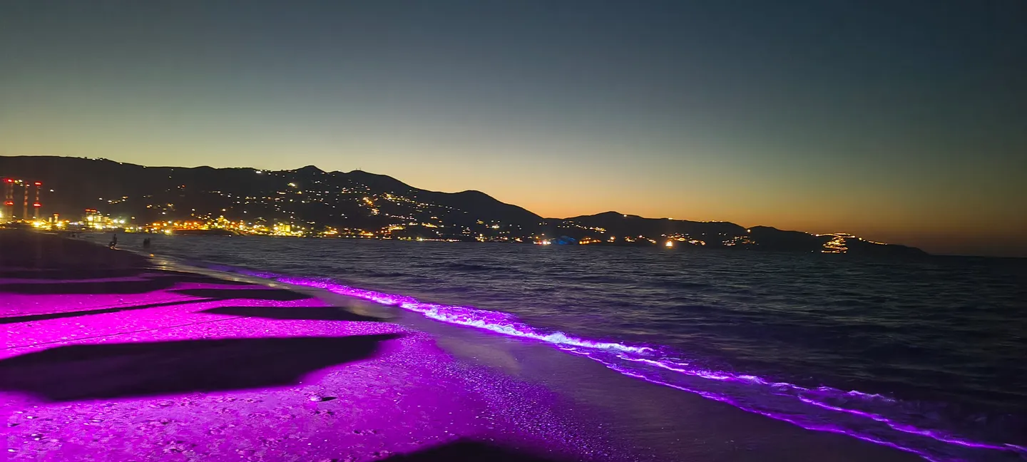 Ammoudara Strand bei Nacht, violett beleuchtet, mit den Lichtern von Heraklion am Horizont