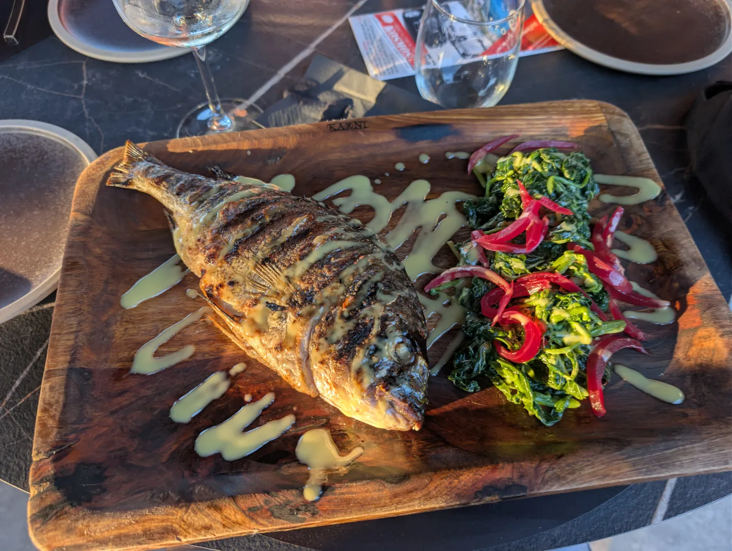 Gegrillte Dorade mit Wildkräutern und roten Zwiebeln auf einem Holzbrett